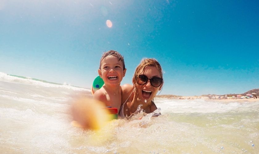 Consejos para cuidar los dientes en verano: mujer con su hijo sonríen bañándose en el mar.