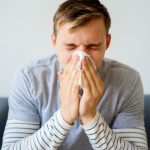 Consejos para cuidar tu boca cuando estás enfermo, resfriado o con gripe: hombre joven sonándose los mocos.