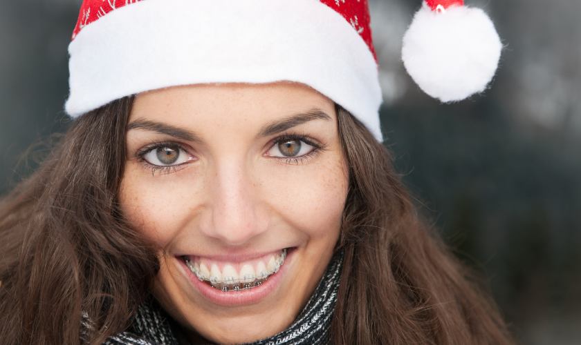 Cuidados específicos para la ortodoncia en Navidad: mujer joven con gorro navideño sonríe mostrando sus brackets.